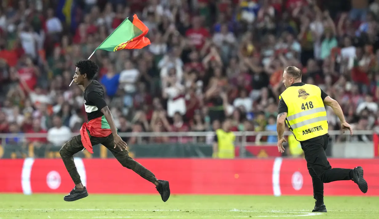 Menyadari petugas keamanan stadion mendekat, suporter penyusup lalu berlari sembari mengibarkan bendera Portugal. (AP Photo/Armando Franca)