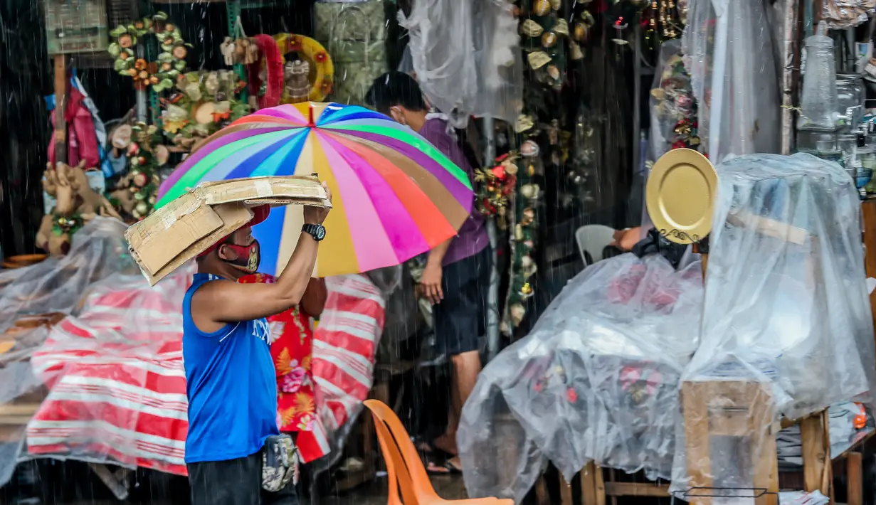 Seorang pria menggunakan kardus sebagai payung saat berjalan melewati banjir di tengah hujan deras yang tiba-tiba mengguyur di sebuah pasar dekorasi Natal di Manila, Filipina (9/12/2020). (Xinhua/Rouelle Umali)