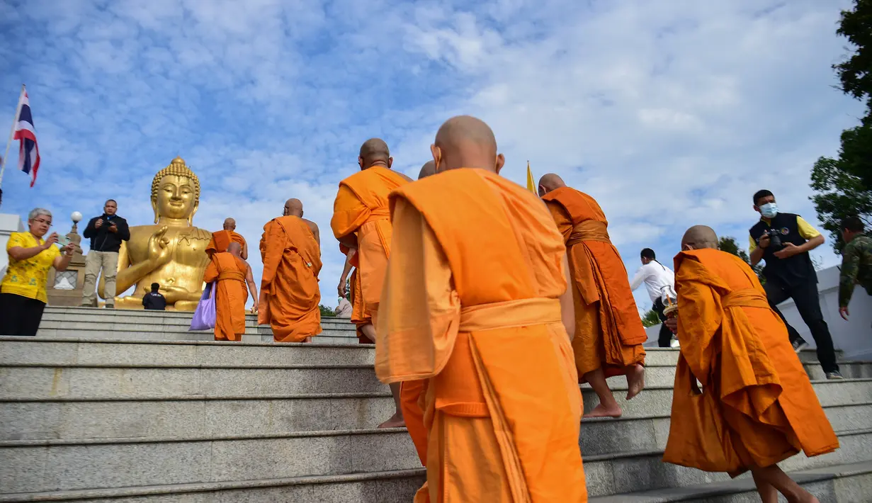 Biksu Buddha berjalan menuju patung Buddha raksasa saat mereka melakukan ritual keagamaan untuk menandai Hari Makha Bucha di kota Narathiwat, Thailand selatan (6/3/2023). Hari raya ini dirayakan pada saat bulan purnama di tiap bulan ketiga kalender Buddha. (AFP/Madaree Tohlala)