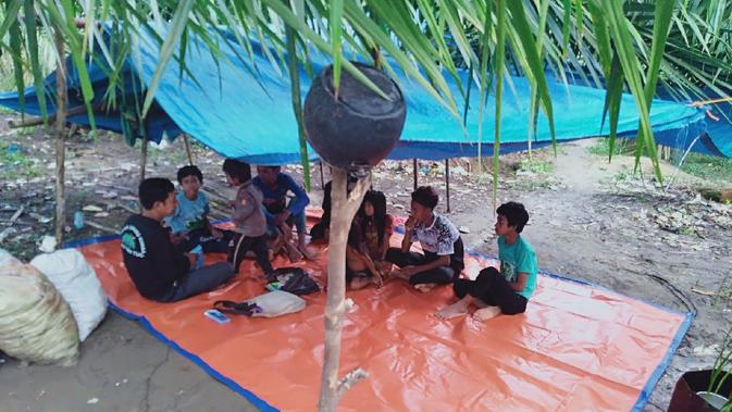 Sejumlah anak-anak rimba belajar bersama Gentar di wilayah Makekal Ilir, Kabupaten Tebo, Jambi, Kamis (19/11/2020). Gentar menjadi salah satu kader pendidikan atau guru alternatif bagi anak-anak rimba di kelompoknya. (Liputan6.com/Gresi Plasmanto)