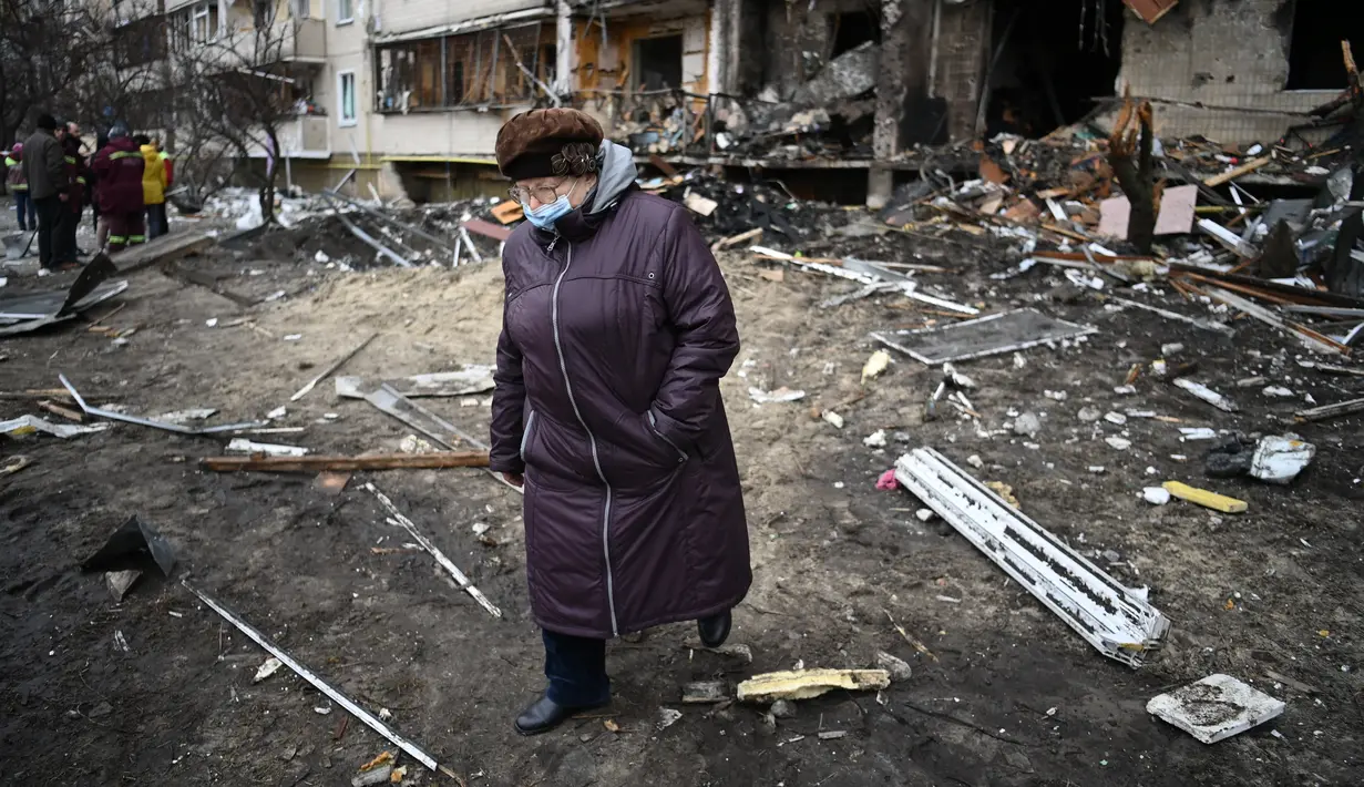 Seorang wanita berjalan di depan bangunan yang rusak setelah peluru militer Rusia menghantam di Koshytsa Street, Kiev, Ukraina (25/2/2022). Ledakan di Kiev memicu kekerasan setelah Presiden Rusia Vladimir Putin menentang peringatan Barat untuk melancarkan invasi darat skala penuh. (AFP/Daniel Leal)