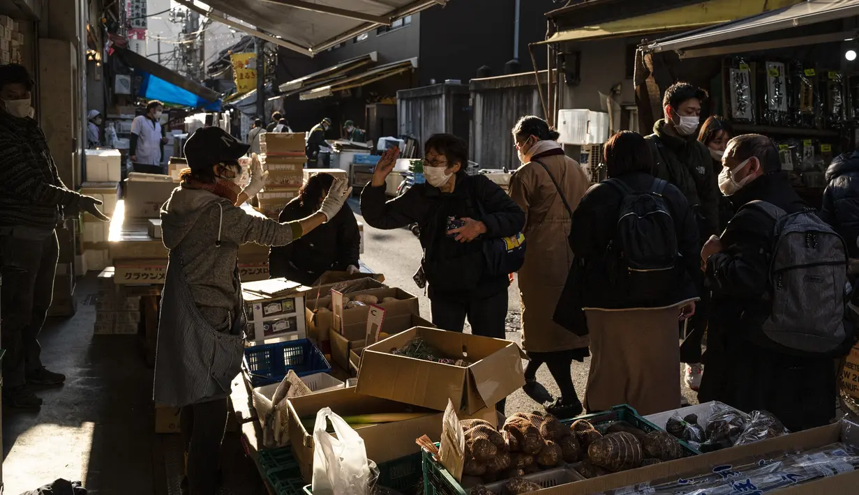 Seorang penjual (kiri) berbicara kepada seorang wanita saat orang-orang berjalan melalui jalan di area "pasar ikan luar" Tsukiji di Tokyo pada 28 Desember 2022. Menjelang liburan Tahun Bar, turis asing dan penduduk lokal berkunjung  ke pasar itu untuk menikmati hidangan bermacam makanan laut. (AFP/Richard A. Brooks)