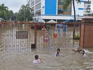 Anak-anak bermain air saat banjir merendam halaman pintu masuk Kantor Direktorat Jenderal Bea dan Cukai di Jakarta, Selasa (25/2/2020). Hujan yang mengguyur Jakarta sejak dini hari tadi membuat halaman Kantor Direktorat Jenderal Bea dan Cukai terendam banjir. (Liputan6.com/Herman Zakharia)