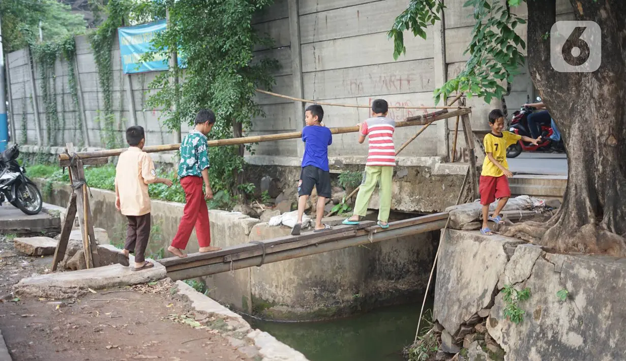 Anak-anak melintasi jembatan saat akan melewati tembok berlubang di Terminal Kampung Rambutan, Jakarta, Kamis (19/12/2019). Jauhnya akses bagi pejalan kaki menjadikan tembok berlubang tersebut pintu alternatif untuk keluar dan masuk Terminal Kampung Rambutan. (Liputan6.com/Immanuel Antonius)