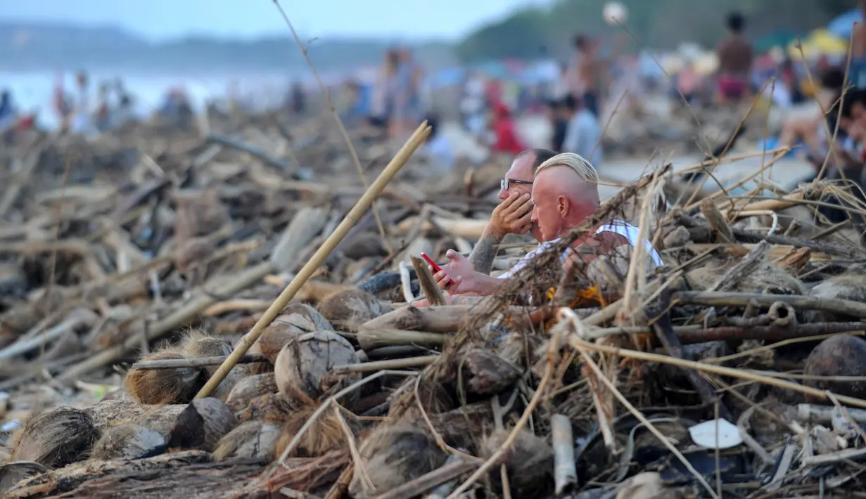 Wisatawan mancanegara duduk di dekat sampah yang terdampar akibat cuaca buruk di Pantai Kuta, Bali, Jumat (15/2). Sampah bervolume besar kembali menepi di Pantai Kuta, kali ini pesisir pantai dipenuhi sampah buah kelapa. (SONNY TUMBELAKA/AFP)