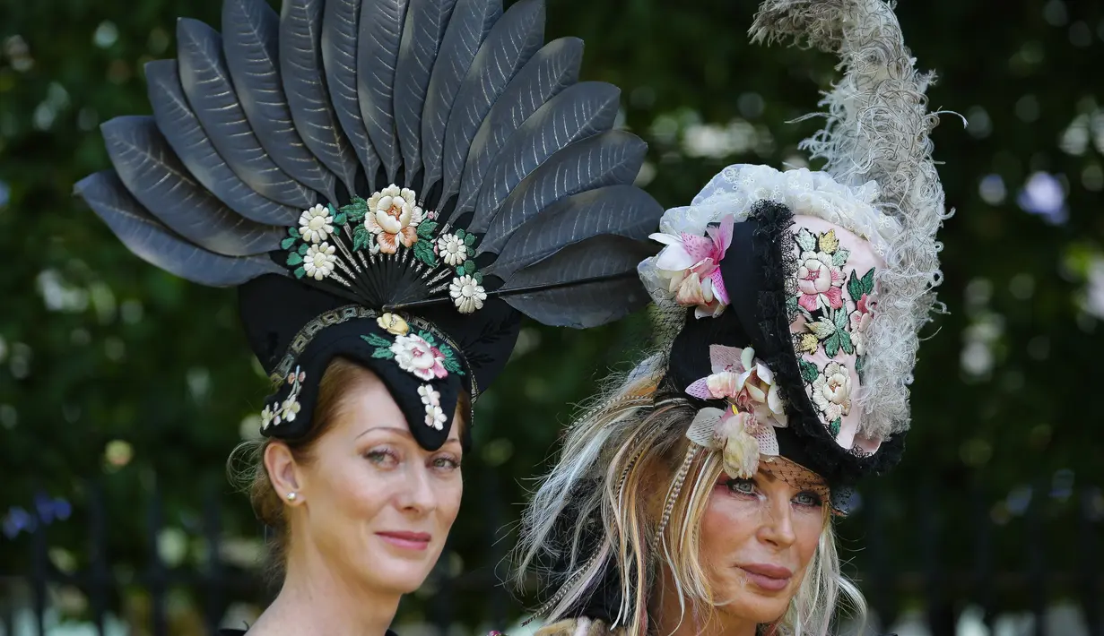 Dua wanita memakai hiasan kepala berpose saat tiba untuk menyaksikan balap kuda Royal Ascot horse di Ascot, London, (20/6). Mereka tampil gaya saat menyaksikan kompetisi balap kuda ini. (AFP Photo/Daniel Leal-Olivas)