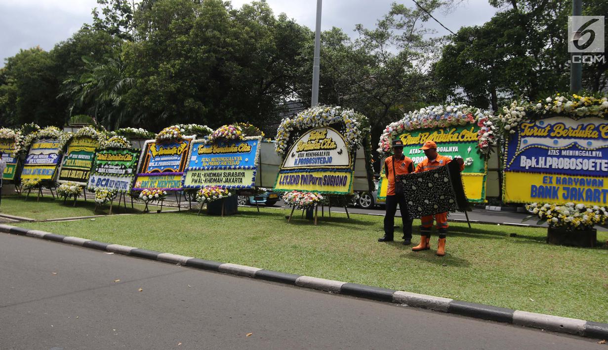 Petugas kebersihan beraktivitas di sekitar karangan bunga ucapan duka cita untuk Probosutedjo di Jalan Diponegoro, Jakarta, Senin (26/3). Probosutedjo merupakan pendiri Himpunan Pengusaha Pribumi Indonesia (Hippi). (Liputan6.com/Arya Manggala)