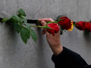Seorang pria meletakkan bunga mawar di tembok selama peringatan runtuhnya Tembok Berlin, di bekas jalur perbatasan antara Berlin Timur dan Berlin Barat, di Bernauer Strasse, pada tanggal 9 November 2023. (Odd ANDERSEN/AFP)