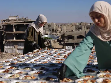 Kakak beradik Palestina, Lina Zeid (kanan) dan Aya Zeid, menyiapkan piring makanan di atap rumah mereka untuk dibagikan kepada anak-anak pengungsi sebagai kegiatan amal di daerah Al-Tuam, sebelah barat Jabalia, Jalur Gaza Utara pada Rabu 6 Mei 2026. (Omar AL-QATTAA/AFP)