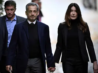 Mantan Presiden Prancis Nicolas Sarkozy (tengah), bersama istrinya Carla Bruni-Sarkozy, berjalan meninggalkan kediamannya untuk menyerahkan diri ke Penjara La Sante guna menjalani hukuman penjara lima tahun setelah dinyatakan bersalah atas konspirasi kriminal terkait rencana pendanaan kampanye pemilu 2007-nya oleh diktator Libya Moamer Kadhafi, di Paris, pada 21 Oktober 2025. (JULIEN DE ROSA/AFP)
