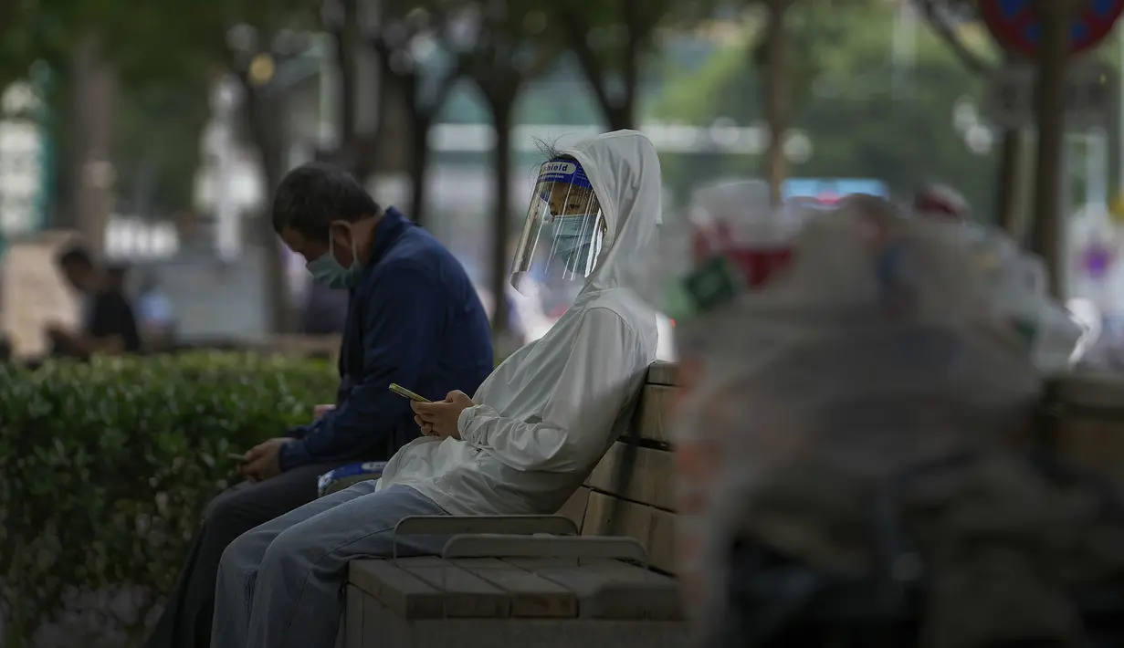 Seorang perempuan yang mengenakan pelindung wajah dan masker beristirahat bersama orang lain di ruang terbuka hijau di Beijing pada Senin, 23 Mei 2022. Beijing memperpanjang perintah bagi pekerja dan siswa untuk tinggal di rumah dan memerintahkan pengujian massal tambahan pada hari Senin untuk membendung kasus COVID-19 yang kembali meningkat di ibu kota China. (AP Photo/Andy Wong)