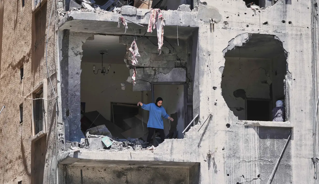 Seorang wanita berjalan melewati apartemennya yang rusak akibat serangan Israel di kota Pelabuhan Tyre, Lebanon Selatan, Kamis 18 Juni 2026. (AP Photo/Hassan Ammar)