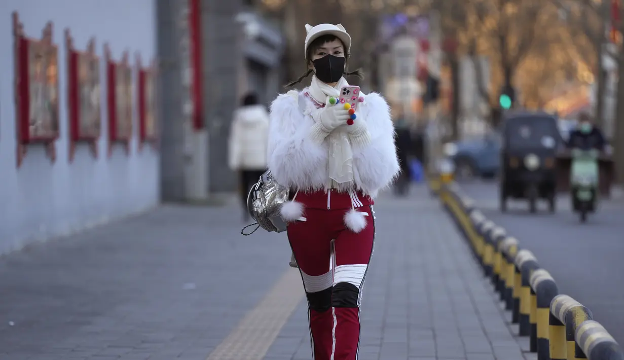 Seorang perempuan mengenakan masker berjalan di jalan Beijing, Jumat, 30 Desember 2022. China berada di jalan terjal untuk kembali ke kehidupan normal ketika warganya kembali ke sekolah, pusat perbelanjaan, dan restoran setelah berakhirnya kebijakan pembatasan paling parah di dunia diakhiri secara tiba-tiba, bahkan ketika rumah sakit dibanjiri pasien Covid-19 yang demam dan meriang parah. (AP Photo/Ng Han Guan)
