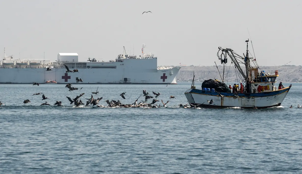 Sebuah kapal nelayan berlayar di dekat kapal rumah sakit Angkatan Laut AS USNS Comfort yang berlabuh di wilayah Piura, Peru, 5 November 2018. Lebih dari 5.000 orang, termasuk imigran Venezuela dirawat oleh personel AS. (ERNESTO BENAVIDES / AFP)