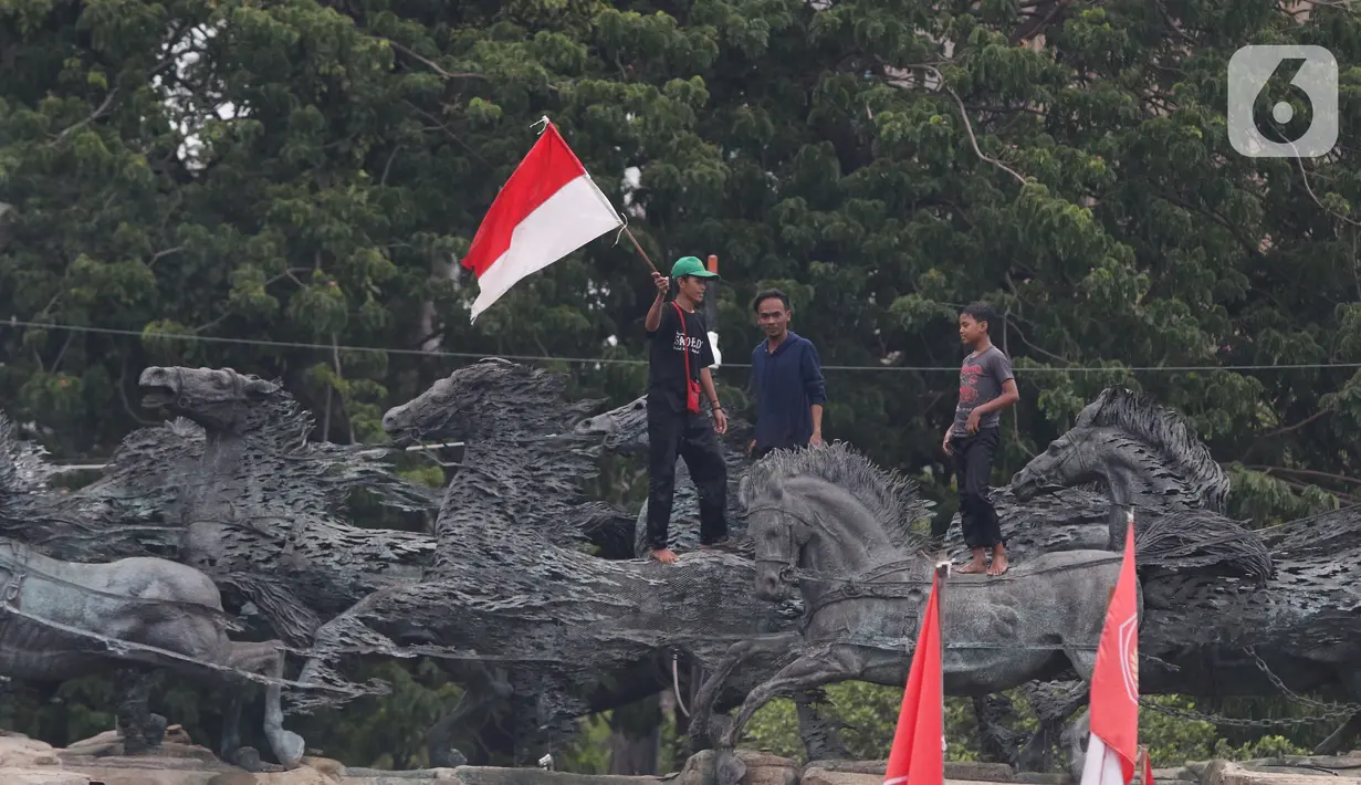 Massa aksi demo tolak omnibus law UU Cipta Kerja naik ke atas patung arjuna wiwaha membawa bendera merah putih di Jalan Medan Merdeka Barat, Jakarta Pusat, Selasa (20/10/2020). Mereka sempat mengibarkan bendera selama kurang lebih lima menit di atas patung. (Liputan6.com/Herman Zakharia)