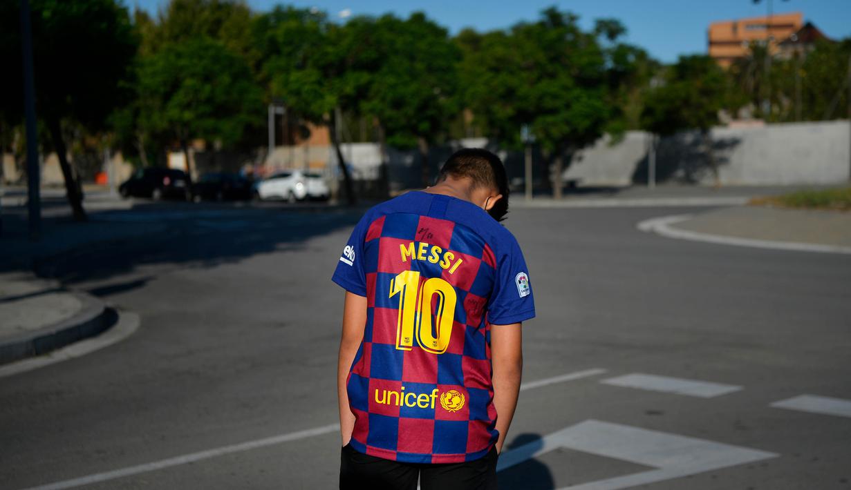 Seorang bocah tertunduk lesu saat menunggu Lionel Messi di lokasi latihan Barcelona, Senin (31/8/2020). Messi secara mengejutkan tidak datang untuk mengikuti tes swab Covid-19 yang dijadwalkan Barcelona. (AFP/Pau Barrena)