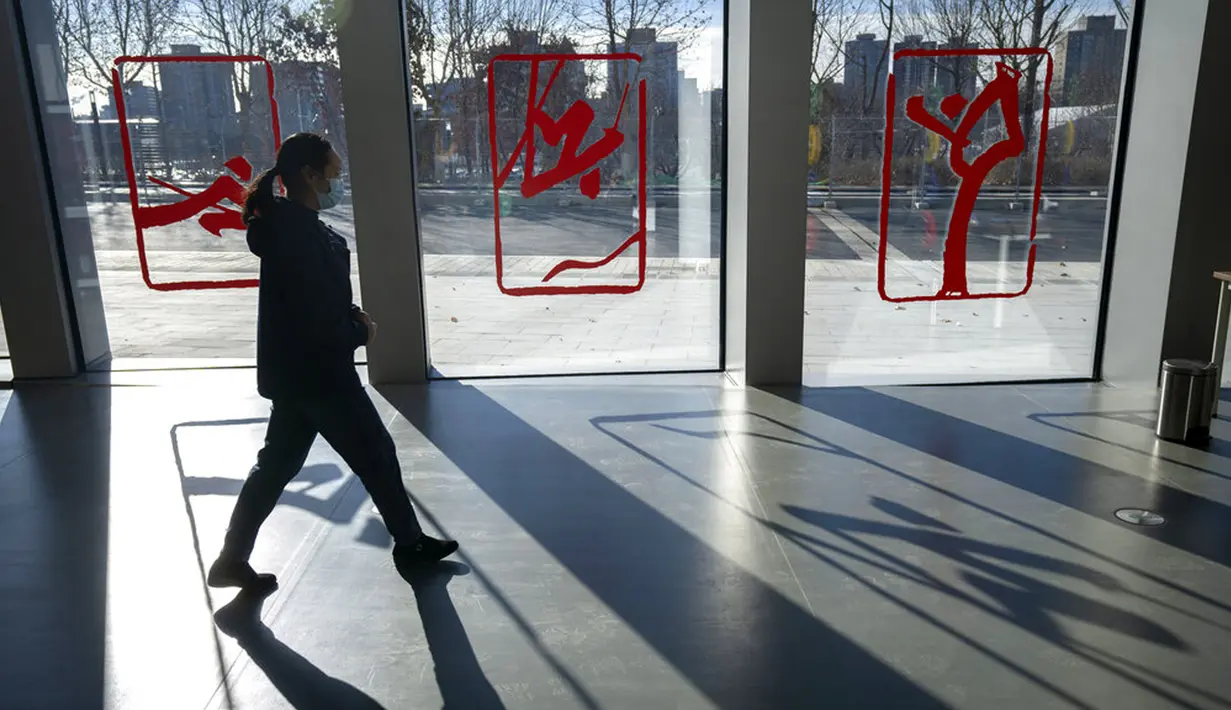 Seorang pekerja berjalan melewati jendela yang didekorasi dengan gambar olahraga musim dingin di Desa Olimpiade Musim Dingin, Beijing, China, Jumat, 24 Desember 2021. Olimpiade dan Paralimpiade Musim Dingin 2022 akan diadakan mulai bulan Februari. (AP Photo/Mark Schiefelbein)