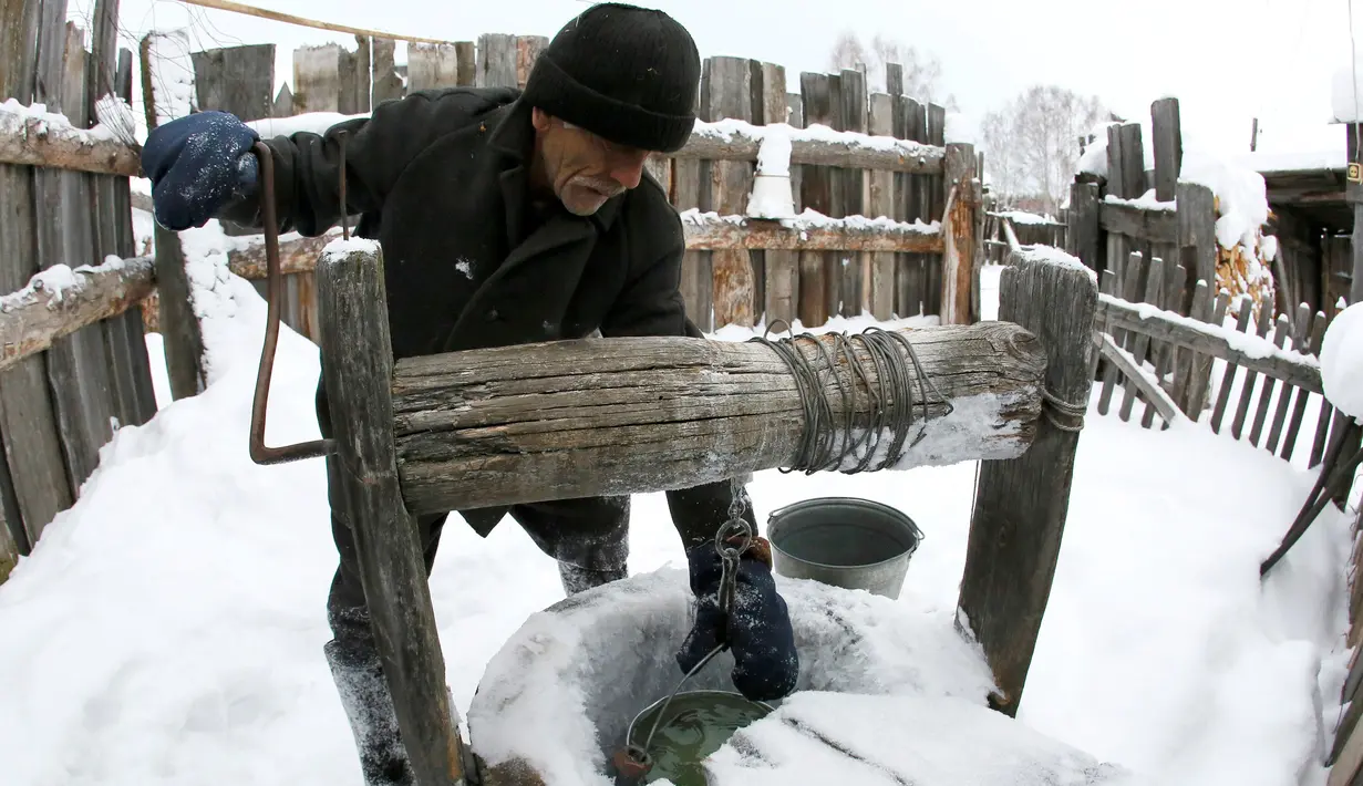 Mikhail Baburin (66) mengambil air dari sumur rumahnya di desa Mikhailovka di Siberia, 5 Desember 2016. Baburin adalah mantan anggota angkatan laut, pekerja Tongkang, dan karyawan pabrik peralatan militer di Krasnoyarsk. (REUTERS/Ilya Naymushin)