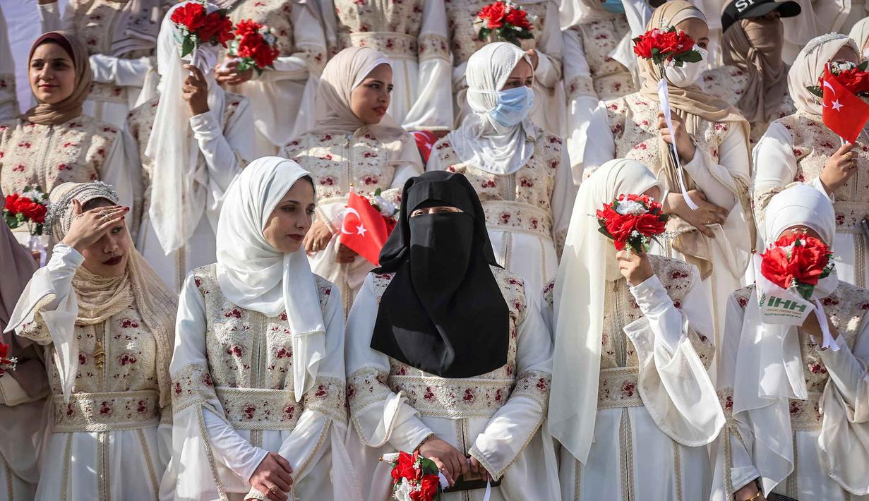 Para pengantin pria dan wanita tampak berkumpul mengenakan busana pernikahan sambil menunggu prosesi dimulai. Tampak dalam foto, para calon pengantin wanita menyaksikan perayaan pernikahan massal untuk pasangan Palestina yang diselenggarakan oleh Yayasan Bantuan Kemanusiaan Turki (IHH) di Kota Gaza pada 11 Mei 2026. (Omar AL-QATTAA/AFP)