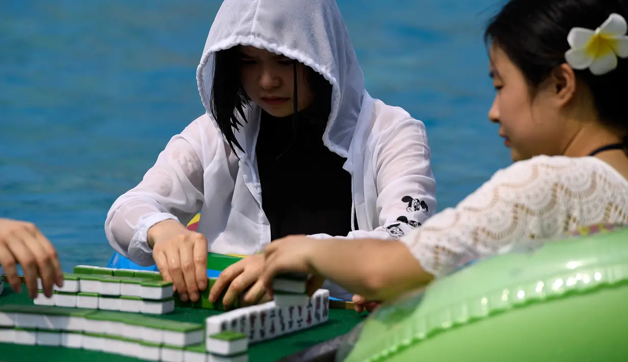 Seorang wanita dan temannya bermain mahjong di dalam kolam renang di Chongqing, Tiongkok, Rabu (2/8). Pemerintah setempat telah mengeluarkan peringatan merah terkait cuaca panas dengan suhu di beberapa daerah hampir mencapai 40 derajat celcius (STR / AFP)
