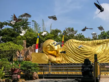 Sejumlah burung merpati terbang di samping patung Buddha raksasa di Maha Vihara Mojopahit, Mojokerto, Jawa Timur, pada tanggal 15 Mei 2024. (JUNI KRISWANTO/AFP)