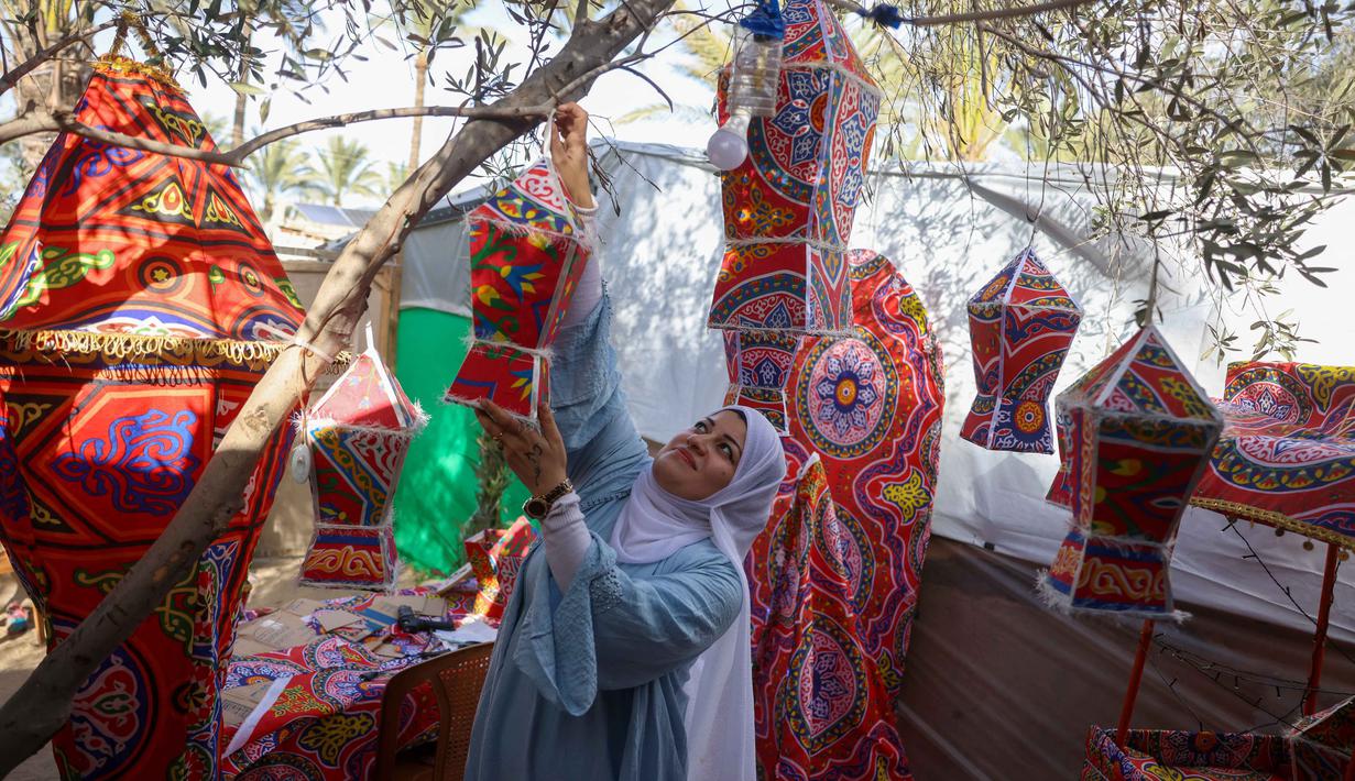 Rehan Hazem Sharab, seorang pengungsi Palestina berusia 32 tahun, menggantung lampion buatan tangan yang terbuat dari kotak-kotak bantuan bekas saat bersiap menyambut bulan suci Ramadan, di luar tendanya di lingkungan Al-Mawasi, Khan Younis, di Jalur Gaza selatan pada Sabtu 7 Februari 2026. Menjelang bulan Ramadan, Rehan Hazem Sharab (32 tahun), seorang perempuan pengungsi yang tinggal di lingkungan Al-Mawasi, Khan Younis, Jalur Gaza selatan, mengubah kardus bantuan dan beberapa kain menjadi lampion Ramadan atau fanous. (Bashar Taleb/AFP)