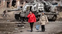 Warga berjalan melewati tank Rusia yang rusak di timur laut kota Trostianets (29/3/2022). Ukraina mengatakan pasukannya telah merebut kembali kota Trostianets, dekat perbatasan Rusia, salah satu kota pertama yang jatuh di bawah Kontrol Moskow dalam invasi selama sebulan. (AFP/Fadel Senna)