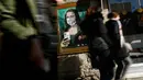 Orang-orang berjalan melewati poster seniman Italia Salvatore Benintende yang menggambarkan Mona Lisa karya Leonardo da Vinci mengenakan masker dan memegang smartphone yang bertuliskan "Mobile World Virus" di sebuah jalan di kota Barcelona, Spanyol pada Selasa (18/2/2020). (PAU BARRENA/AFP)