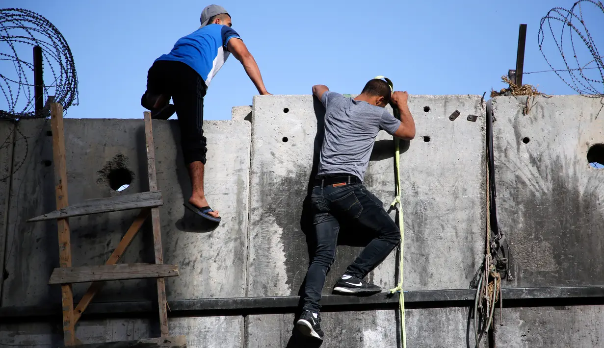 Dua pemuda Palestina menggunakan tangga berusaha memanjat tembok pembatas Israel saat berangkat untuk beribadah salat Jumat di Masjid Al-Aqsa, Yerusalem, Jumat (9/6). (AFP Photo/Abbas Momani)