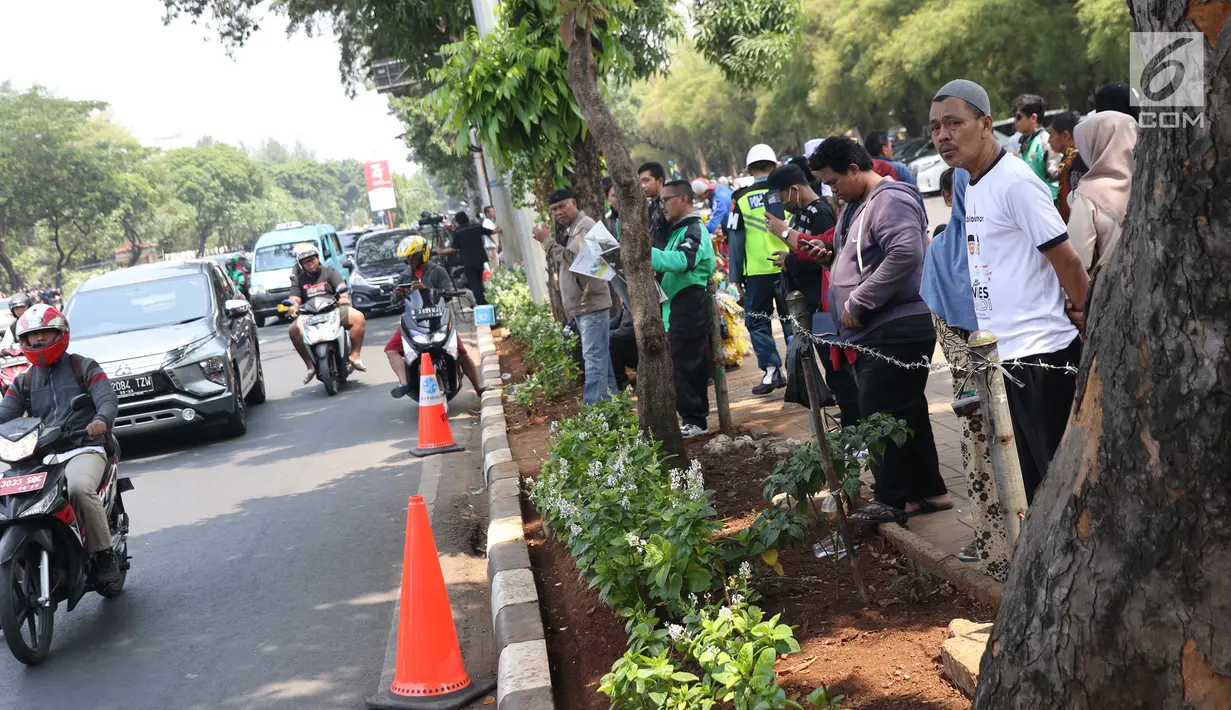 Sejumlah warga berdiri di sisi jalan TMP Kalibata untuk melihat prosesi pemakaman Presiden RI ke-3 BJ Habibie, Jakarta, Kamis (12/9/2019). BJ Habibie meninggal dunia setelah menjalani perawatan di RSPAD dan akan dimakamkan di Taman Makam Pahlawan Kalibata. (Liputan6.com/Helmi Fithriansyah)