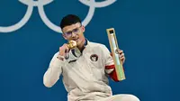 Lifter Indonesia, Rizki Juniansyah, merengkuh medali emas angkat besi kelas 73 kg putra pada Olimpiade Paris 2024 di South Paris Arena, Jumat (9/8/2024) dini hari WIB. (Miguel Medina/AFP)