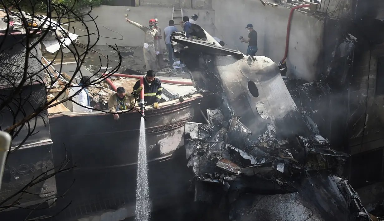 Petugas pemadam kebakaran menyemprotkan air pada puing pesawat Pakistan International Airlines yang jatuh di Karachi, Pakistan, Jumat (22/5/2020). Menurut perwakilan dari Kementerian Kesehatan Sindh, 97 orang dilaporkan meninggal dan dua orang selamat dalam kecelakaan tersebut. (Rizwan TABASSUM/AFP)