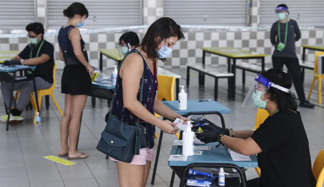 Pemilih mengenakan masker saat memverifikasi identitas dengan petugas pemilu di TPS Sekolah Tinggi Chung Cheng, Singapura, Jumat (10/7/2020). Pemilu di tengah pandemi COVID-19, warga Singapura memberikan suara mereka dengan mengenakan masker dan sarung tangan plastik. (AP Photo)