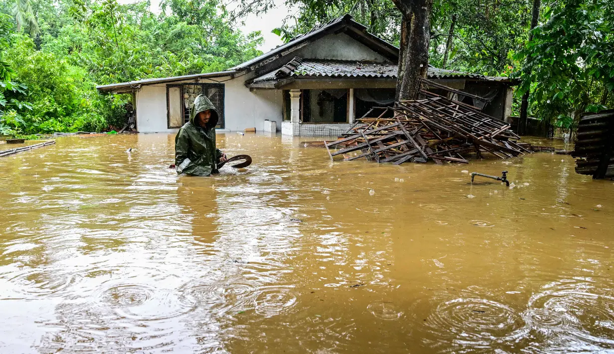 Warga di distrik-distrik tersebut diimbau untuk tetap waspada, menghindari perjalanan yang tidak perlu, dan bersiap untuk evakuasi segera. Tampak dalam foto, seorang pria mengarungi banjir di luar rumahnya setelah hujan deras di Kaduwela, pinggiran Kolombo, pada Jumat 28 November 2025. (Ishara S. KODIKARA/AFP)