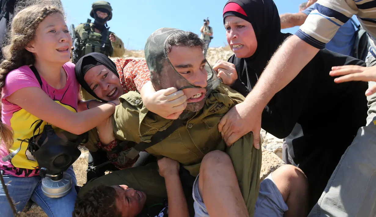 Foto yang diambil pada 28 Agustus 2015, Ahed Tamimi (kiri) berkelahi melawan tentara Israel saat terjadi bentrokan di Desa Nabi Saleh. Saat itu Ahed menggigit dan menampar tentara Israel yang menangkap saudara laki-lakinya. (AFP Photo/Abbas Momani)