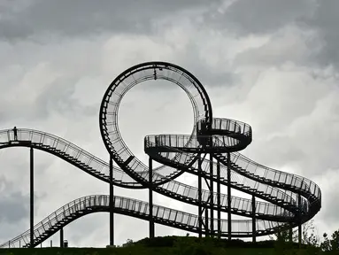 Orang-orang berjalan di sebuah instalasi tangga melingkar "Tiger and Turtle" di Duisburg, Jerman, 30 April 2018. Instalasi seni ini adalah patung jalan setapak menyerupai roller coaster yang berada di atas puncak bukit. (AP/Martin Meissner)