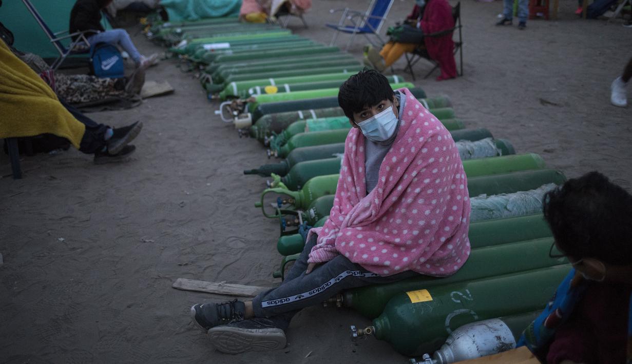 Seorang pria duduk di atas tabung oksigen kosong saat menunggu toko buka untuk mengisi tabung mereka di Villa El Salvador, Lima, Peru, Selasa (6/4/2021). Warga Peru terus berjuang mendapatkan oksigen medis untuk merawat pasien COVID-19. (AP Photo/Rodrigo Abd)