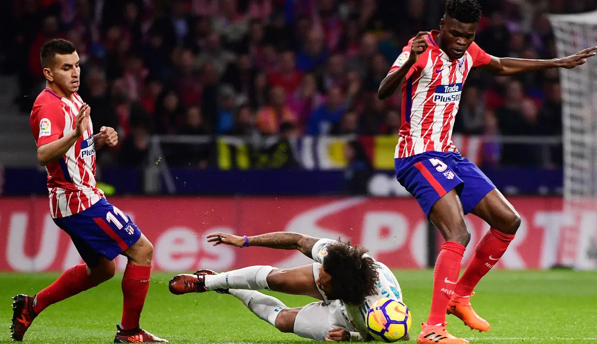 Pemain Real Madrid, Marcelo terjatuh dekat pemain Atletico Madrid, Thomas (R) dan Angel Correa pada laga pekan ke-12 La Liga di Stadion Wanda Metropolitano, Sabtu (18/11). Laga Derbi Madrid itu berakhir imbang tanpa gol (PIERRE-PHILIPPE MARCOU/AFP)