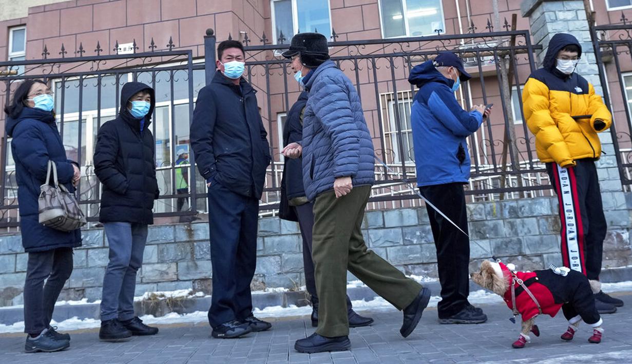 Seorang pria berjalan dengan seekor anjing melewati warga yang mengantre untuk tes COVID-19 di Distrik Fengtai, Beijing, China, Rabu (26/1/2022). Jelang Olimpiade Musim Dingin, Beijing melaporkan peningkatan lebih dari selusin kasus baru COVID-19 setiap harinya. (AP Photo/Andy Wong)