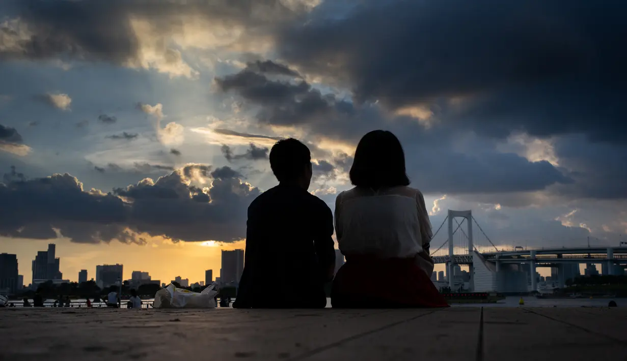 Pasangan menikmati matahari terbenam di Odaiba, Tokyo, (29/7). Odaiba merupakan salah satu tujuan wisata di Tokyo, sekaligus lokasi pusat perbelanjaan dan permukiman. (AFP Photo/Martin Bureau)