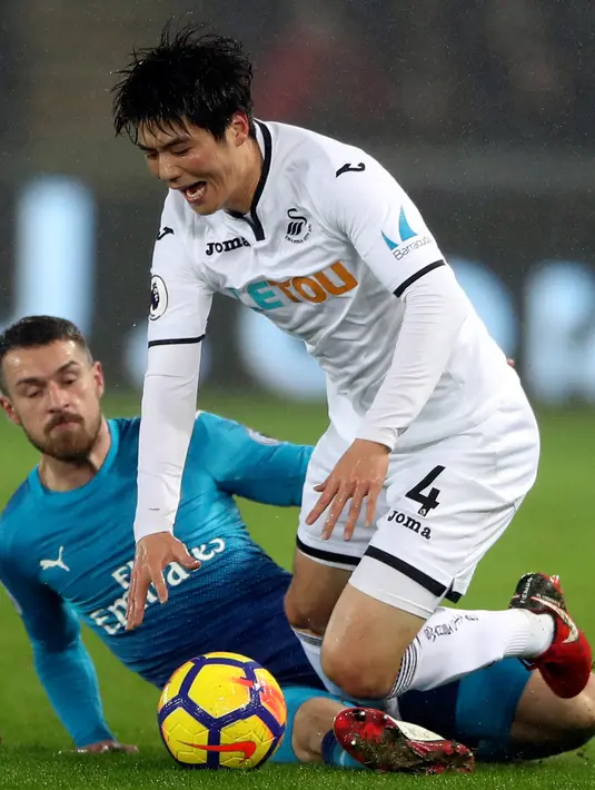 Pemain Arsenal, Aaron Ramsey berebut bola dengan pemain Swansea City, Ki Sung-yueng dalam laga pekan ke-25 Premier League 2017-2018 di Liberty Stadium, Selasa (30/1). Arsenal dipaksa menyerah Swansea City 1-3. (Nick Potts/PA via AP)