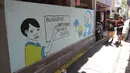 Anak-anak melintasi mural di Kampung Budaya Kawasan Jakarta Barat, Selasa (19/11/2019). Penataan dilakukan mulai daari pembenahan jalan, pembuatan resapan air, bangku, mural, hingga ubin pemandu untuk penyandang disabilitas dengan anggaran mencapai Rp2.5 miliar. (Liputan6.com/Herman Zakharia)