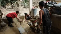Pembersihan rumah dan barang-barang dilakukan agar mereka dapat segera kembali ke rumah setelah mengungsi. Tampak dalam foto, Panji (kanan), 23 tahun, membawa lumpur keluar dari dapur menggunakan gerobak dorong di rumah orang tuanya, setelah banjir bandang, di Aceh Tamiang, Minggu 14 Desember 2025. (Yasuyoshi CHIBA/AFP)