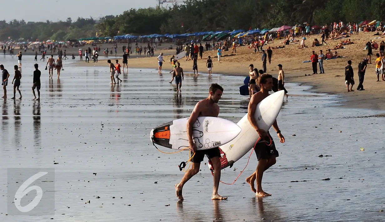Beberapa wisatawan melintas usai bermain surfing di kawasan Pantai Kuta, Bali, 31 Agustus 2015. Pantai Kuta masih menjadi lokasi wisata utama bagi wisatawan yang berkunjung ke Bali. (Liputan6.com/Helmi Fithriansyah)