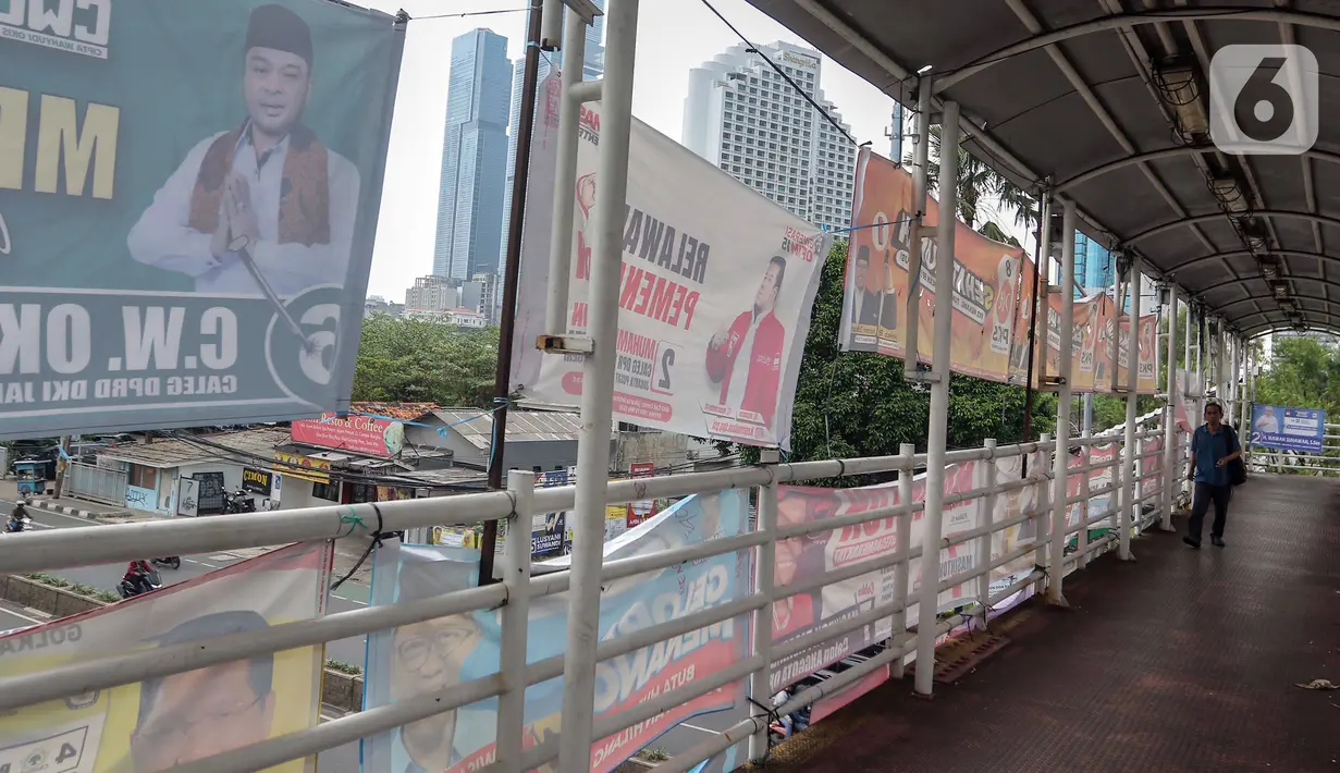 Warga berjalan meewati JPO yang dipenuhi alat peraga kampanye di Jakarta. (Liputan6.com/Angga Yuniar)