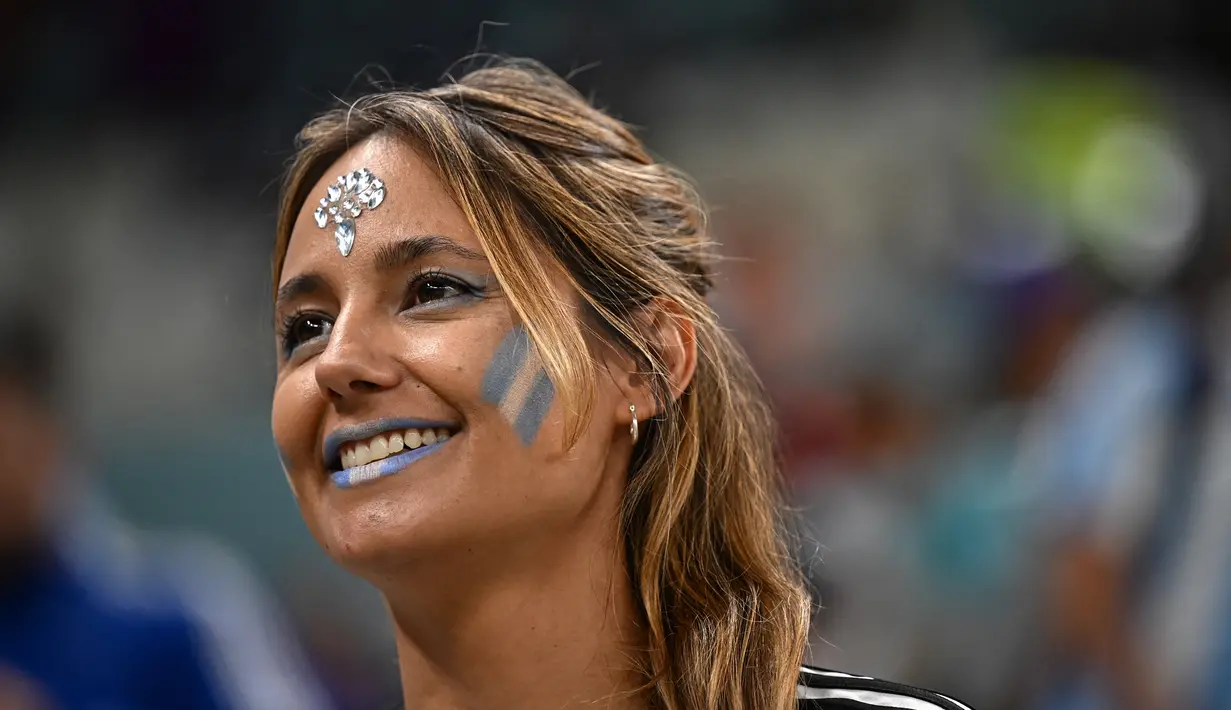 Seorang fans wanita Argentina tersenyum di tribun menjelang pertandingan semifinal Piala Dunia Qatar 2022 antara Argentina dan Kroasia di Stadion Lusail di Lusail, utara Doha, Rabu (14/12/2022). (AFP/ Anne-Christine Poujoulat)