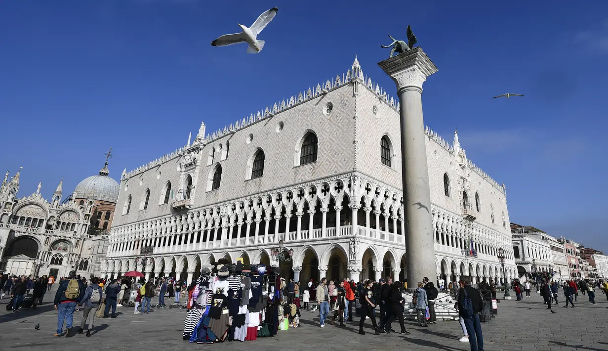 Wisatawan berjalan melintasi Lapangan Santo Markus dengan latar Basilika Santo dan Istana Doge di Venesia, Italia (4/11/2019). (AFP Photo/Miguel Medina)