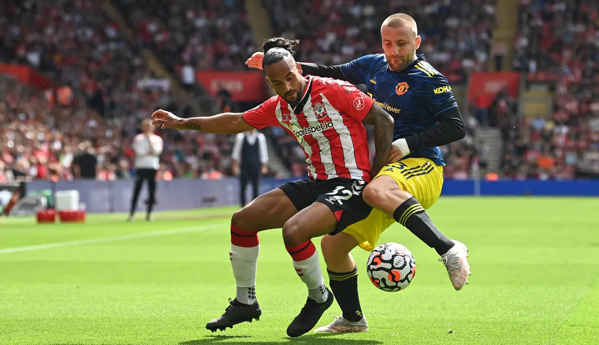 Pemain Manchester United Luke Shaw (kanan) berebut bola dengan pemain Southampton Theo Walcott (tengah) pada pertandingan Liga Inggris di Stadion St Mary, Southampton, Inggris, 22 Agustus 2021. Pertandingan berakhir imbang 1-1. (Glyn KIRK/AFP)