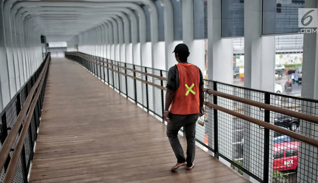 Pekerja berjalan di jembatan penyeberangan orang (JPO) Bundaran Senayan, Jakarta, Senin (21/1). Bagian lantai JPO Bundaran Senayan dilapisi kayu artificial agar tidak licin dan bebas lapuk. (Liputan6.com/Faizal Fanani)