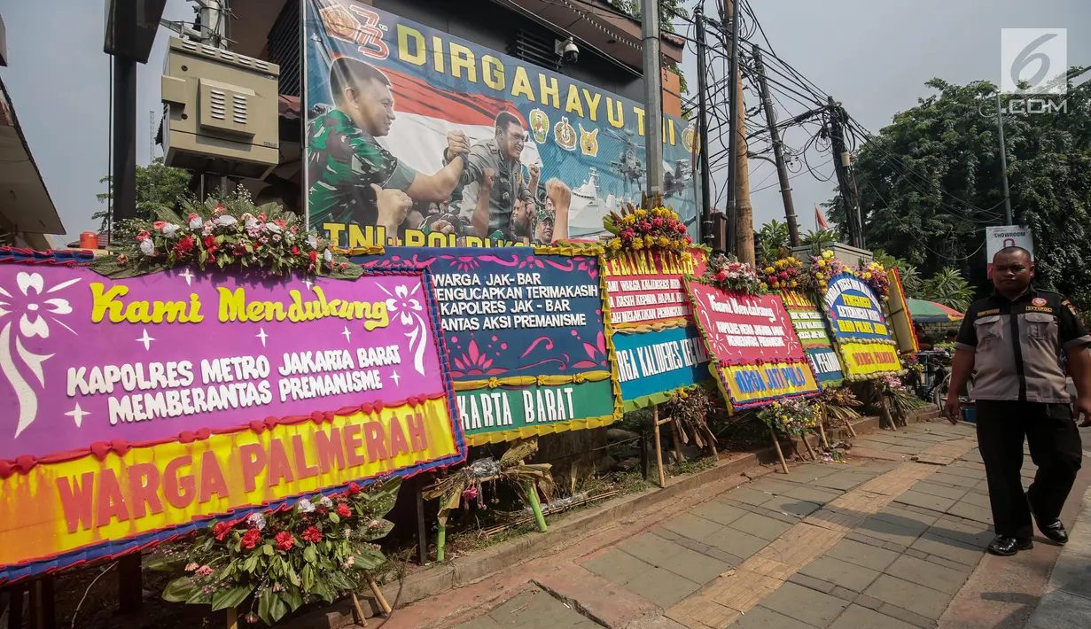 Warga melintasi karangan bunga di Halaman Polres Jakarta Barat, Jumat (23/11). Puluhan karangan bunga yang dikirimkan warga tersebut diberikan guna mendukung pihak kepolisian dalam memberantas aksi premanisme di Jakarta Barat. (Liputan6.com/Faizal Fanani)